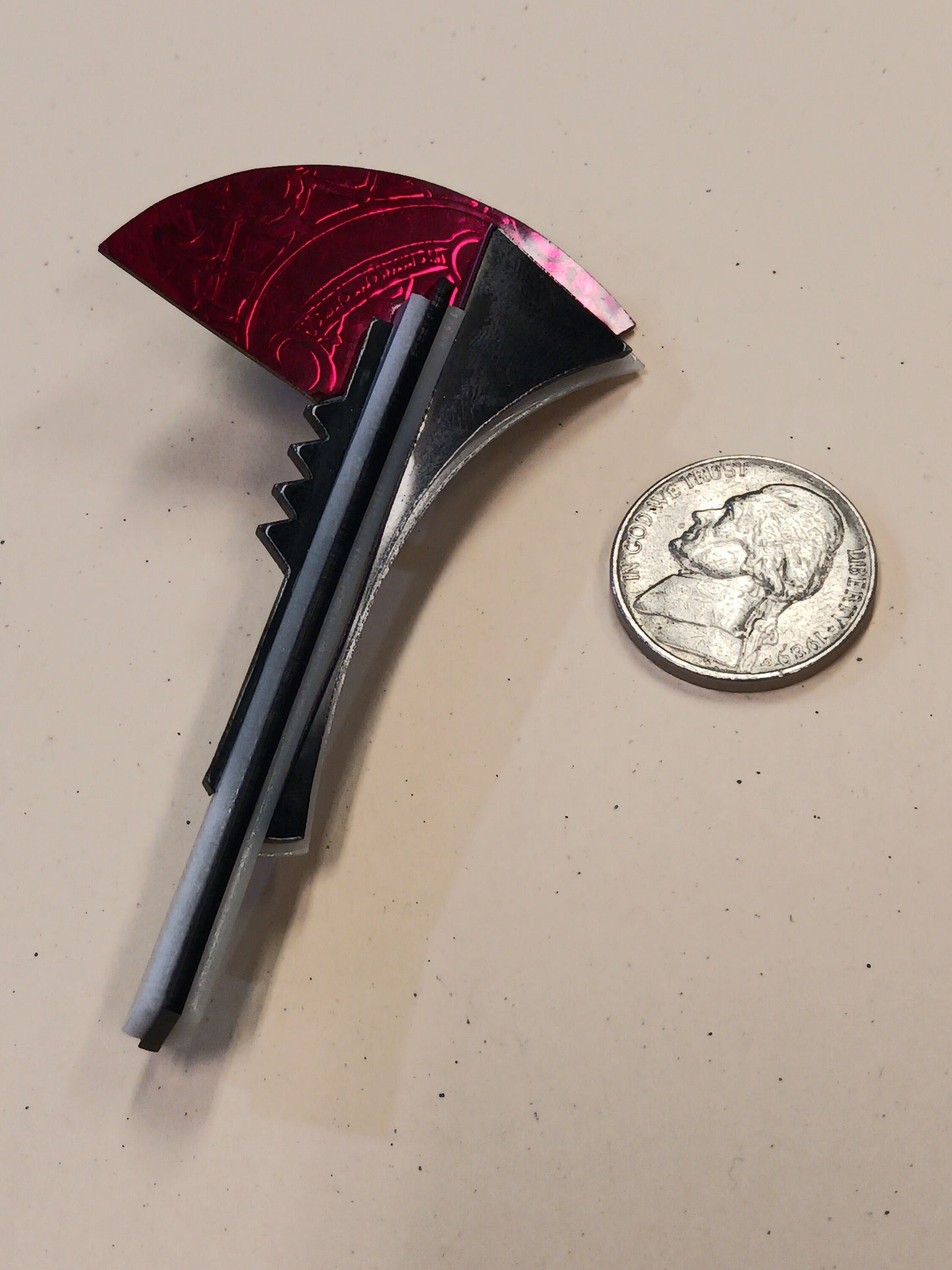 Brooch with red and black design next to a quarter on a beige surface
