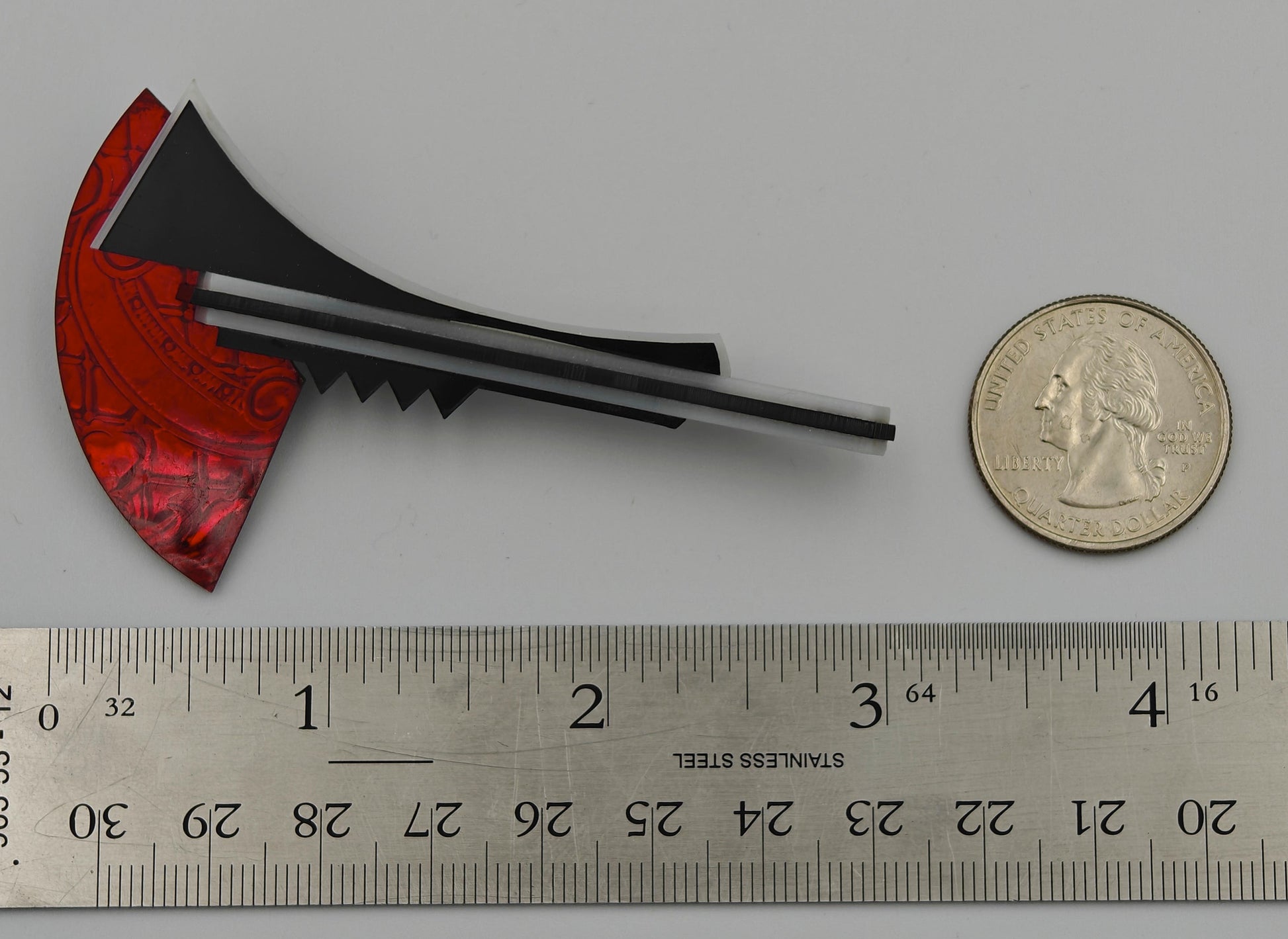 Brooch next to a ruler and coin on a gray background