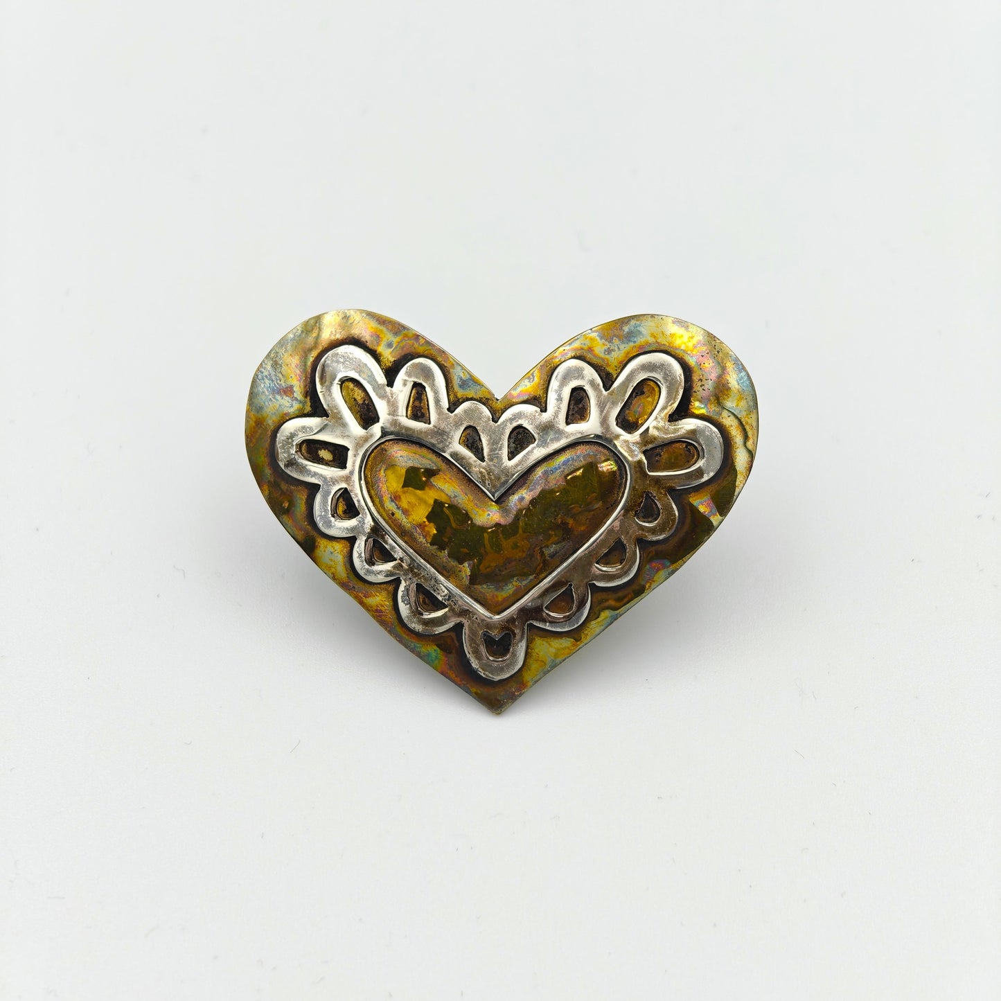 Heart-shaped metal scarf tie with intricate design on a white background