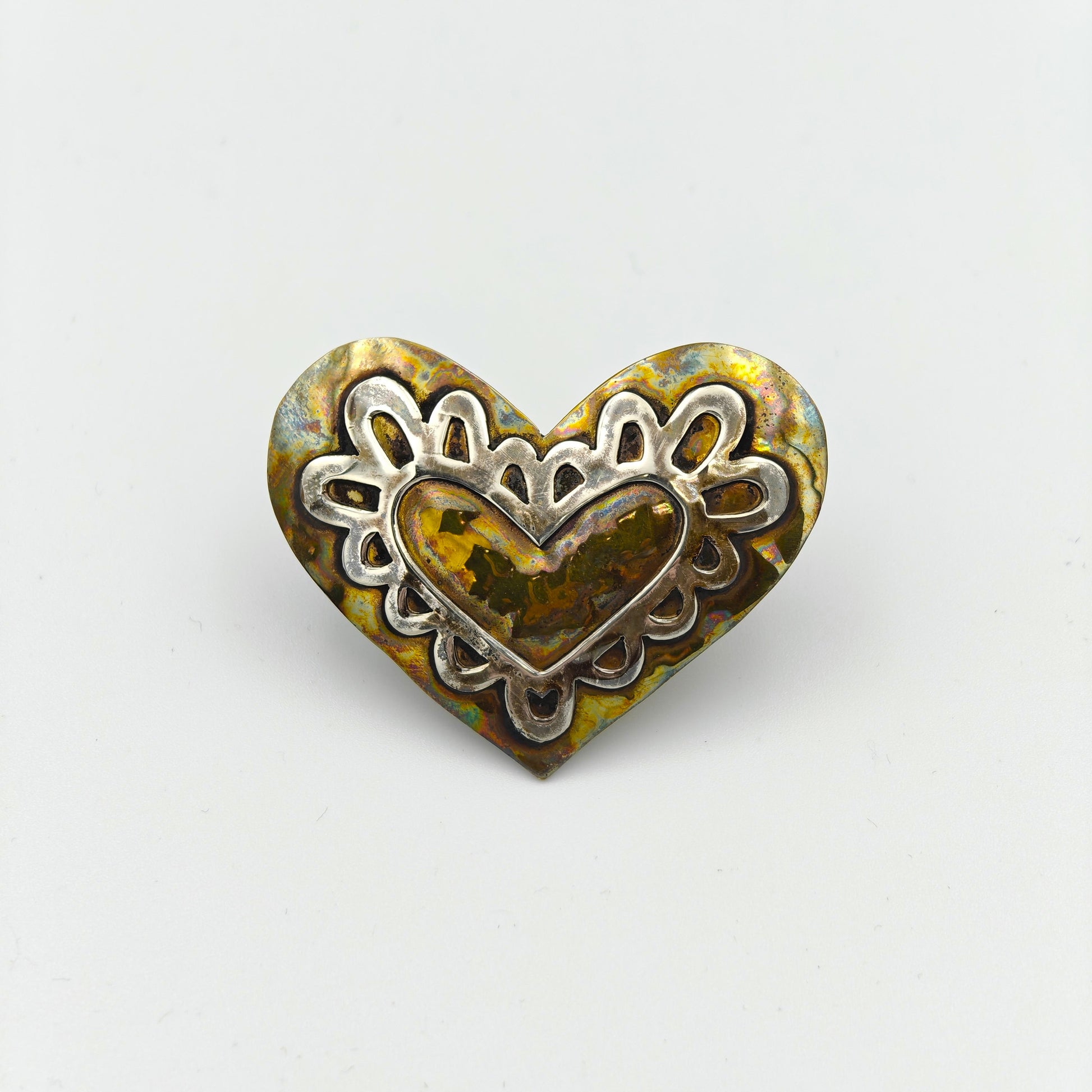 Heart-shaped metal scarf tie with intricate design on a white background