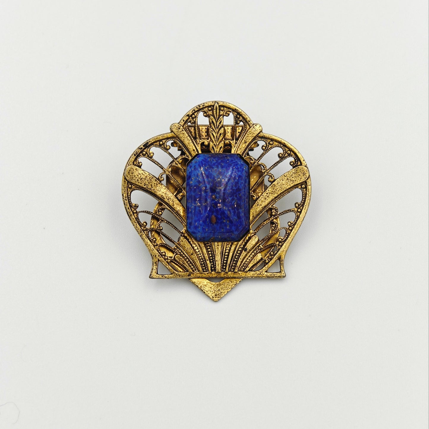 Gold brooch with a blue gemstone on a white background