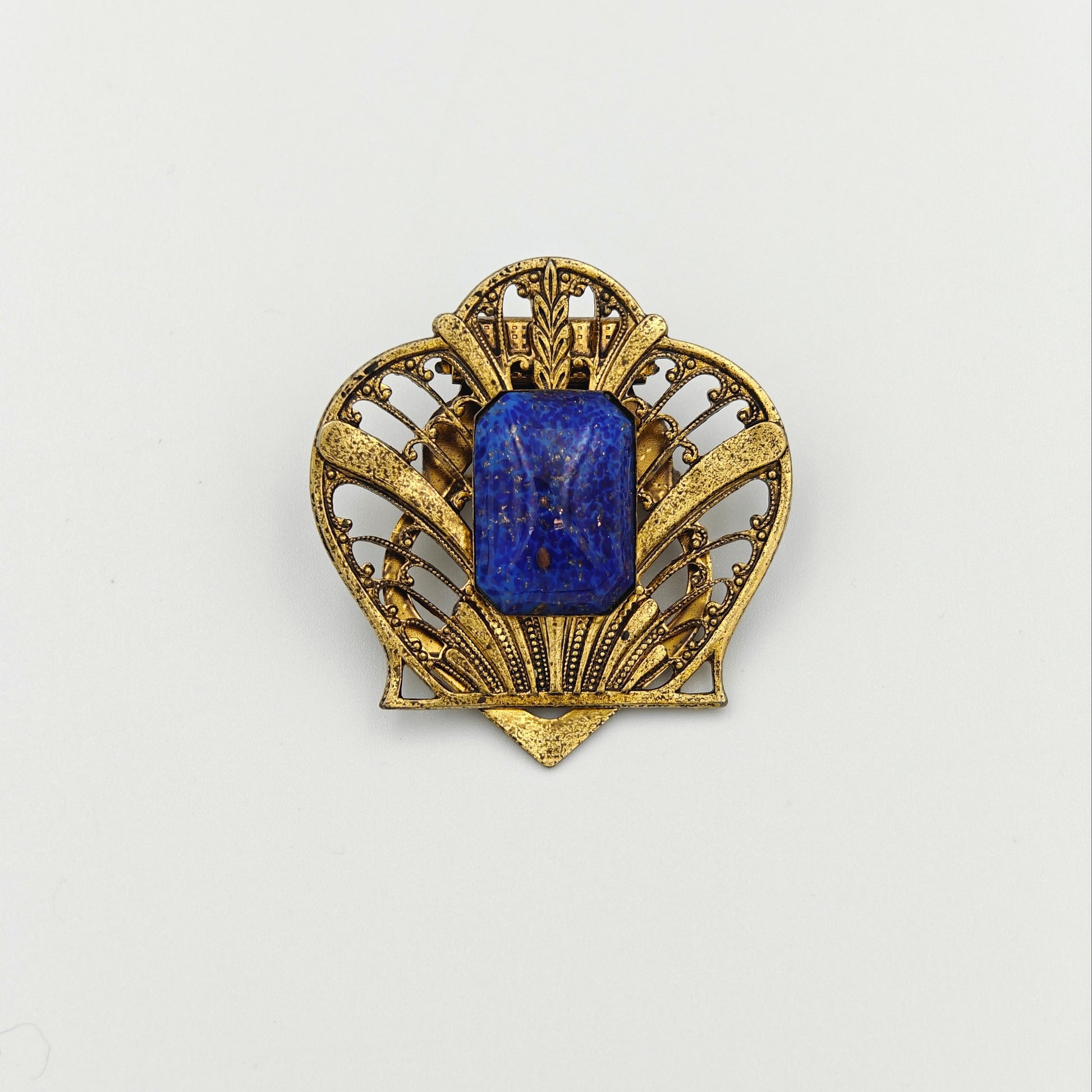 Gold brooch with a blue gemstone on a white background