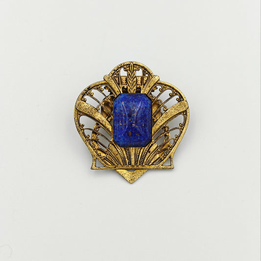 Gold brooch with a blue gemstone on a white background