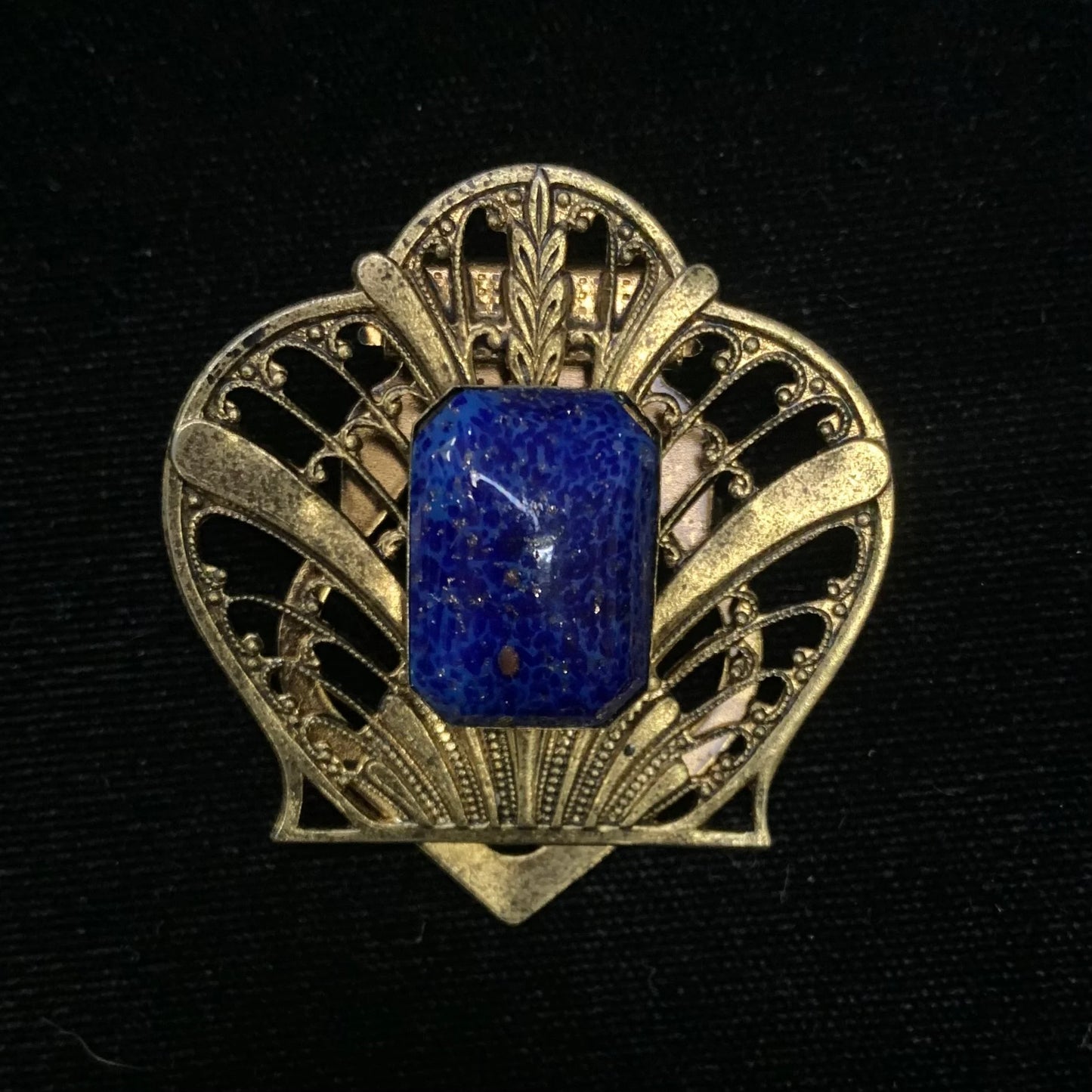 Gold brooch with a blue stone on a black background