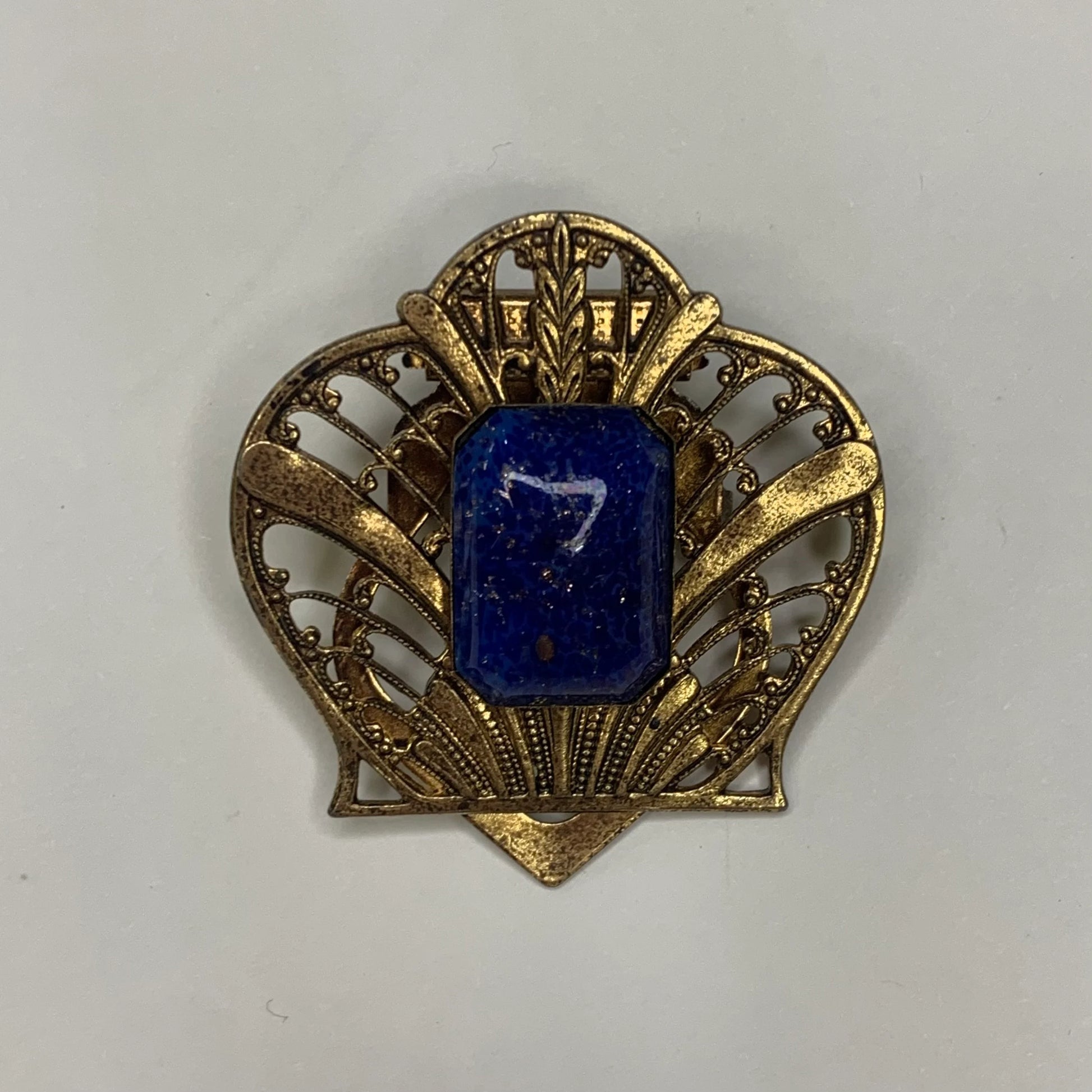 Gold brooch with a blue central stone on a white background
