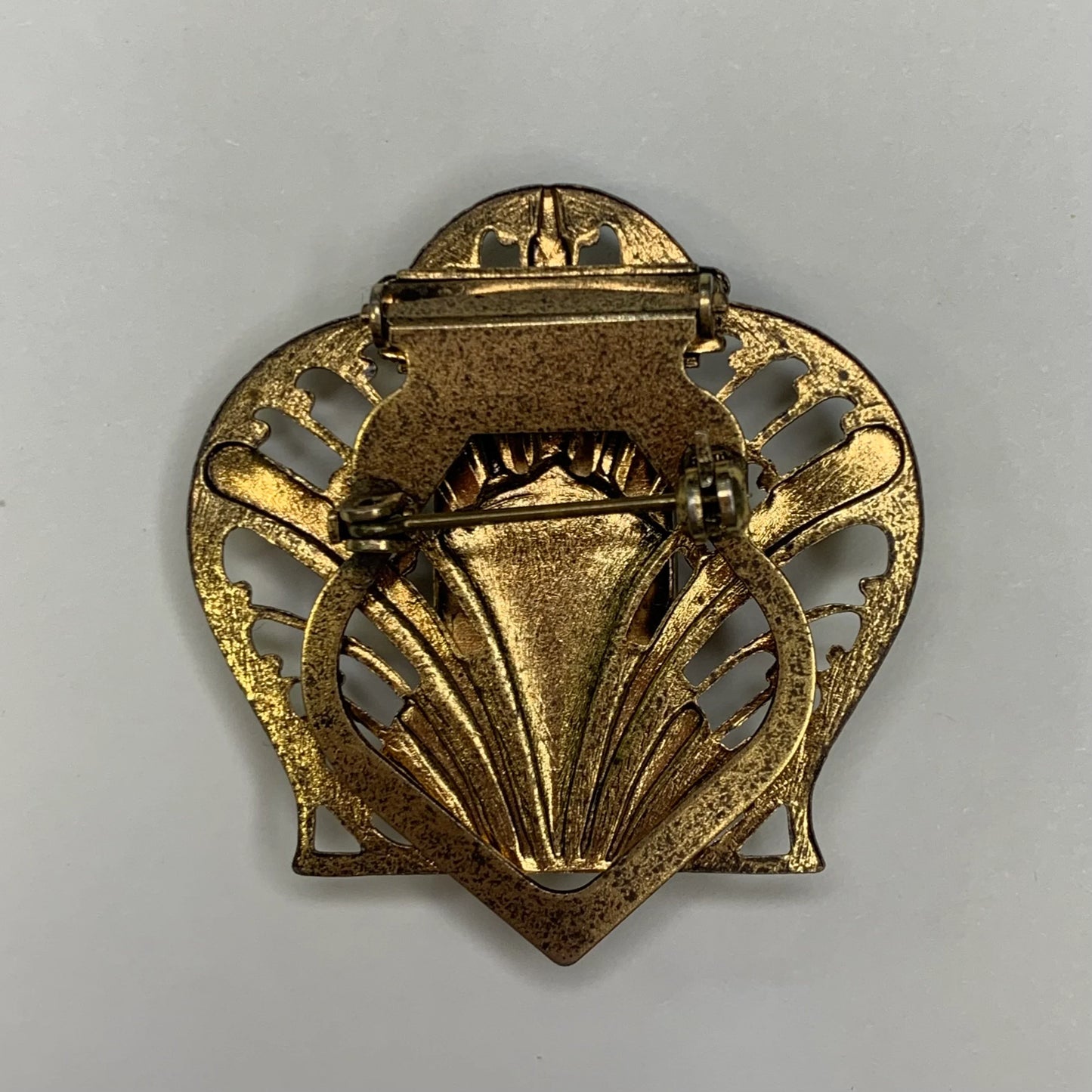 Back of gold brooch with intricate design on a gray background