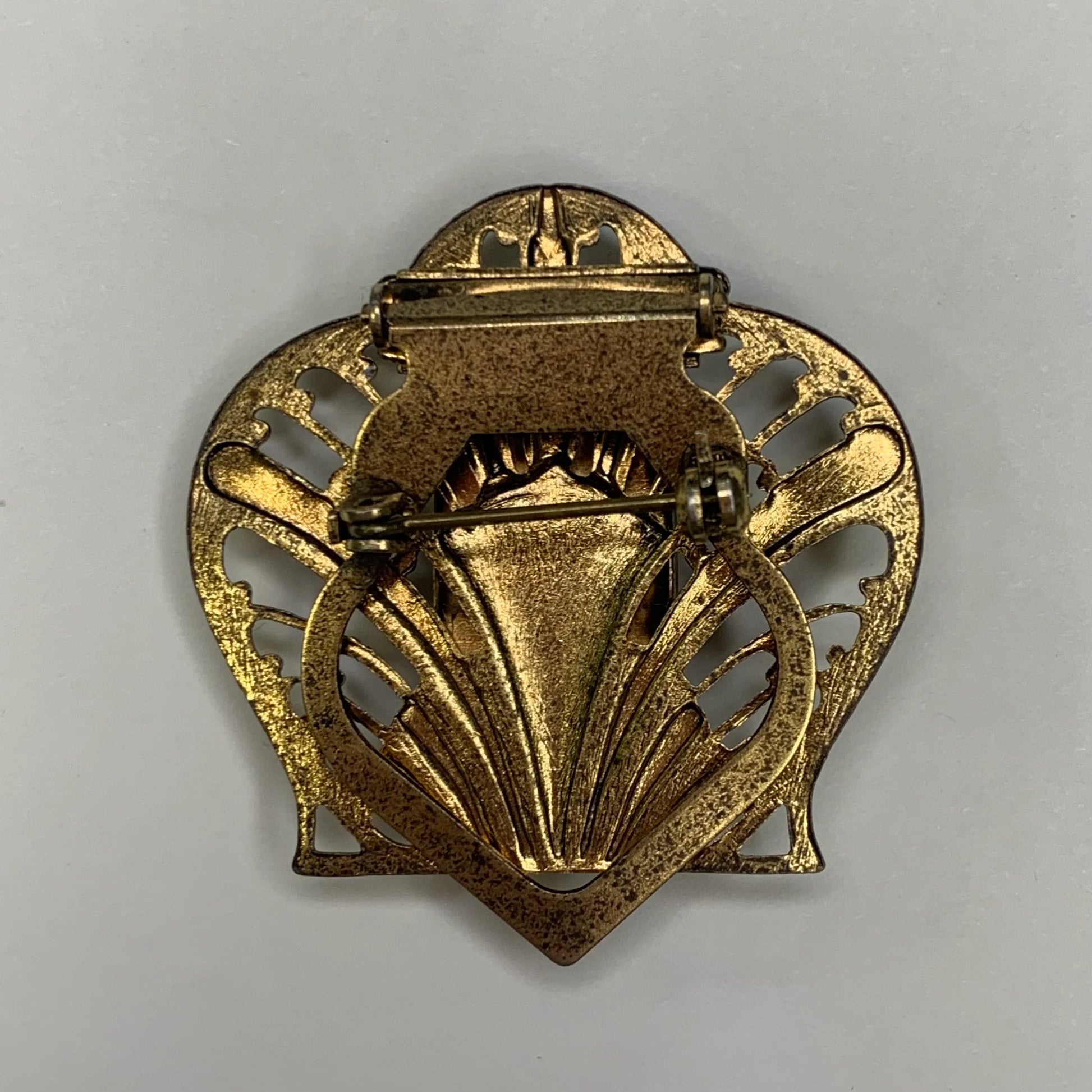 Back of gold brooch with intricate design on a gray background