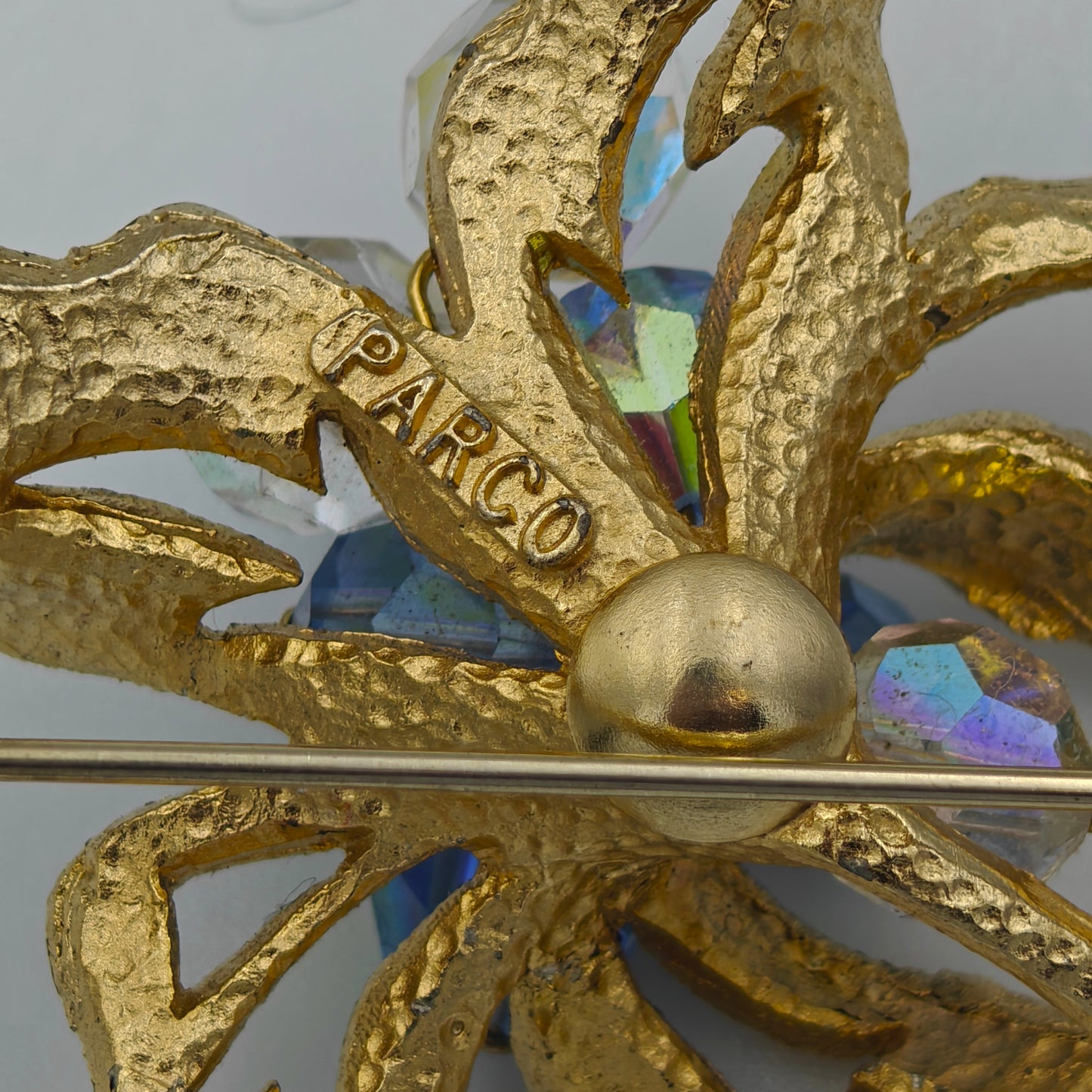 Decorative gold brooch with intricate design and multicolored gemstones on a light gray background