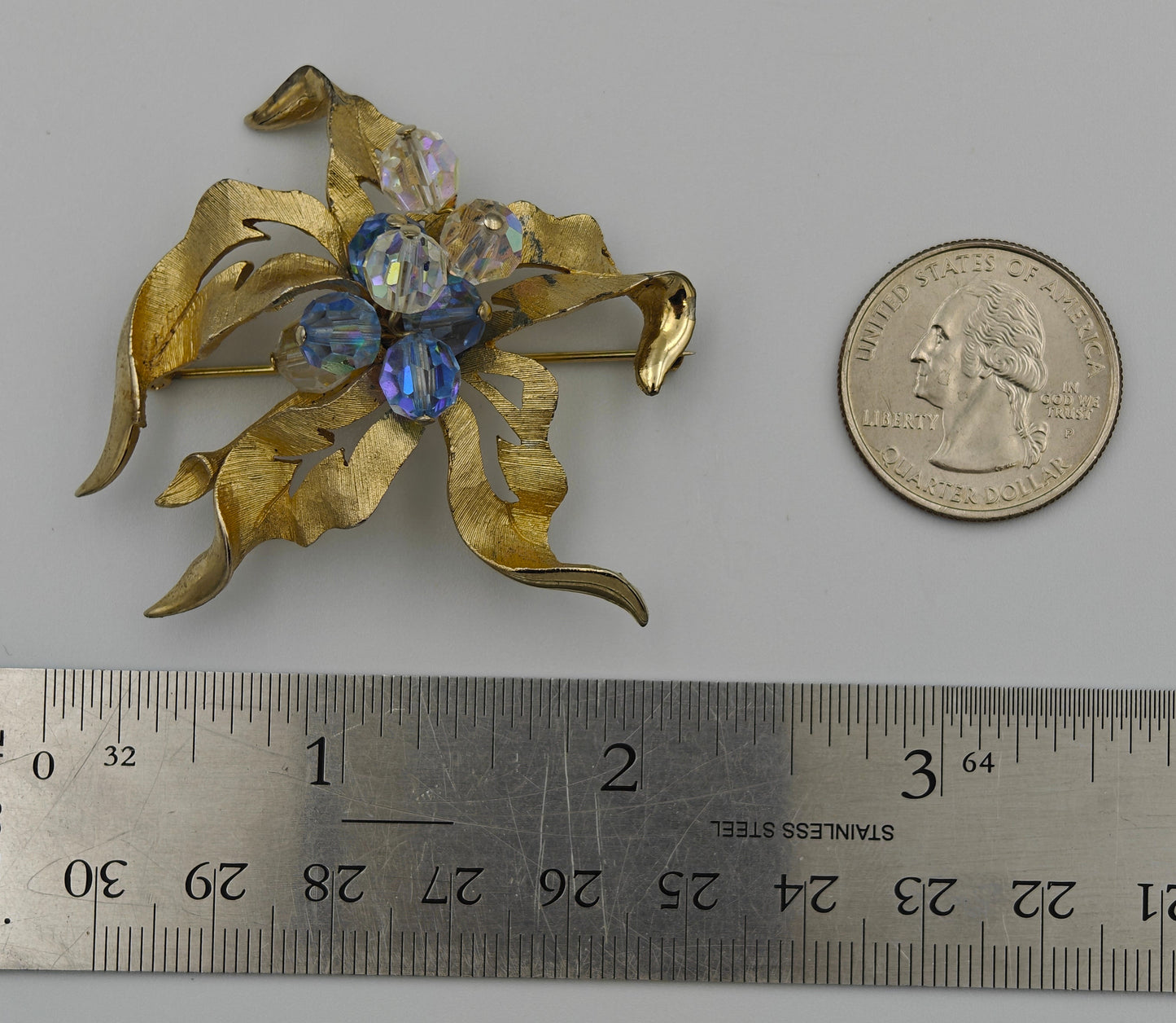 Gold brooch with gemstones next to a ruler and quarter for scale on a gray background