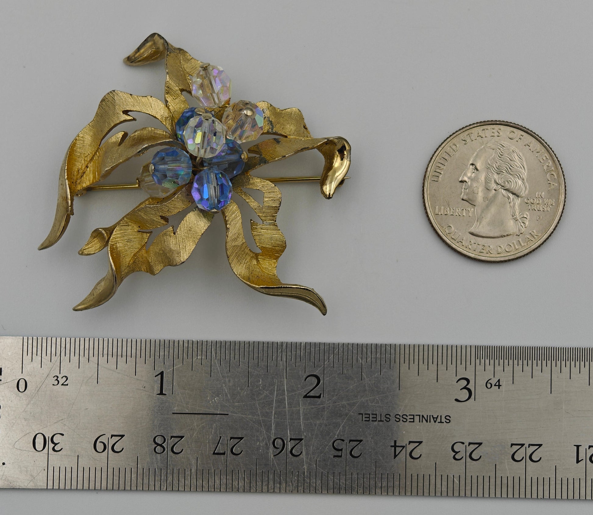 Gold brooch with gemstones next to a ruler and quarter for scale on a gray background