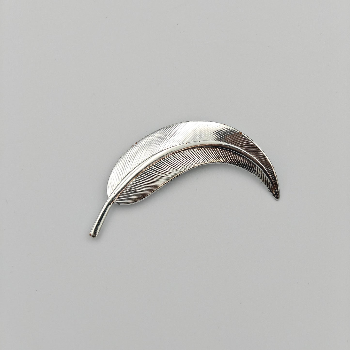 Silver feather-shaped brooch on a white background