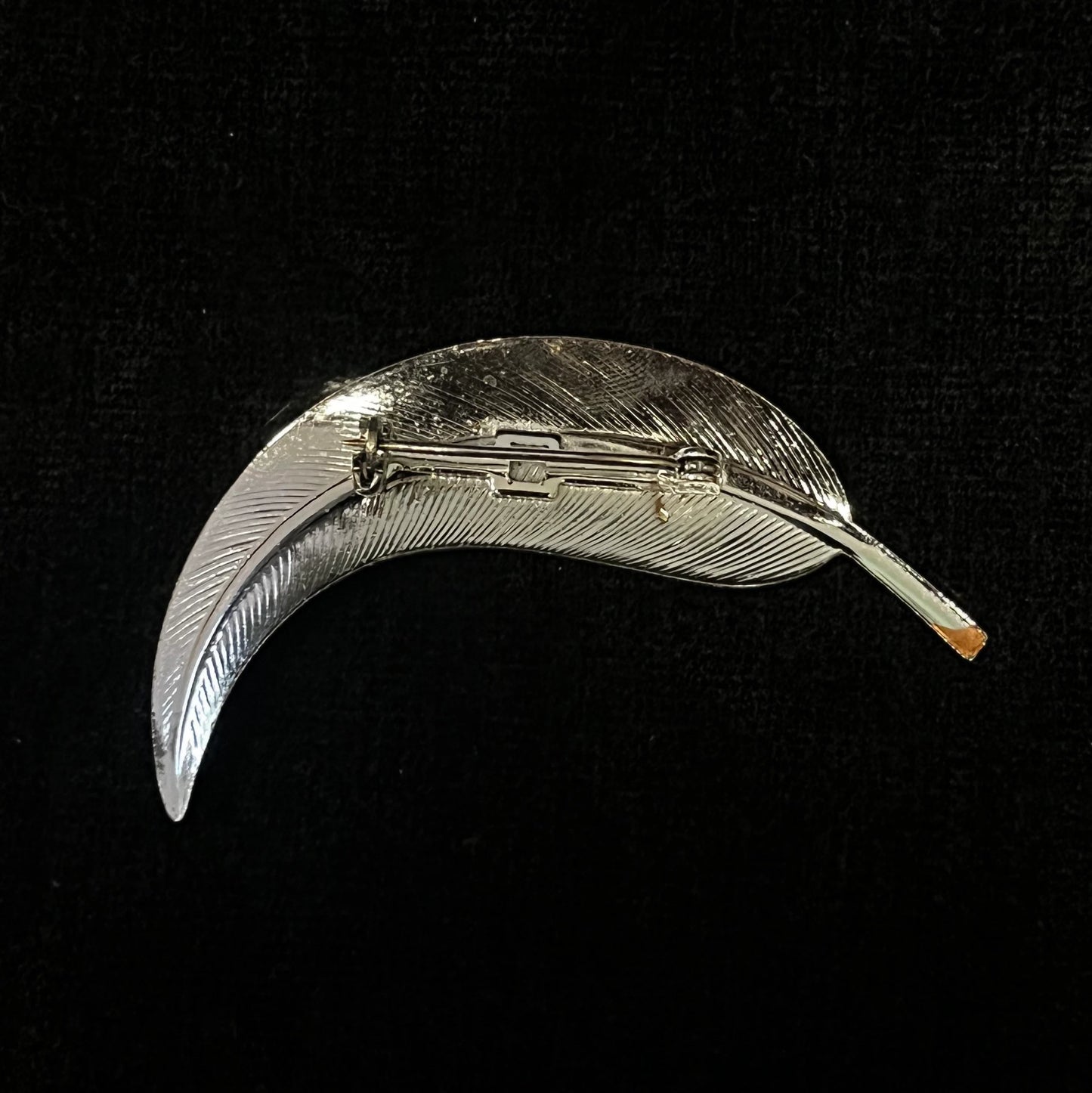 Silver feather-shaped brooch on a black background
