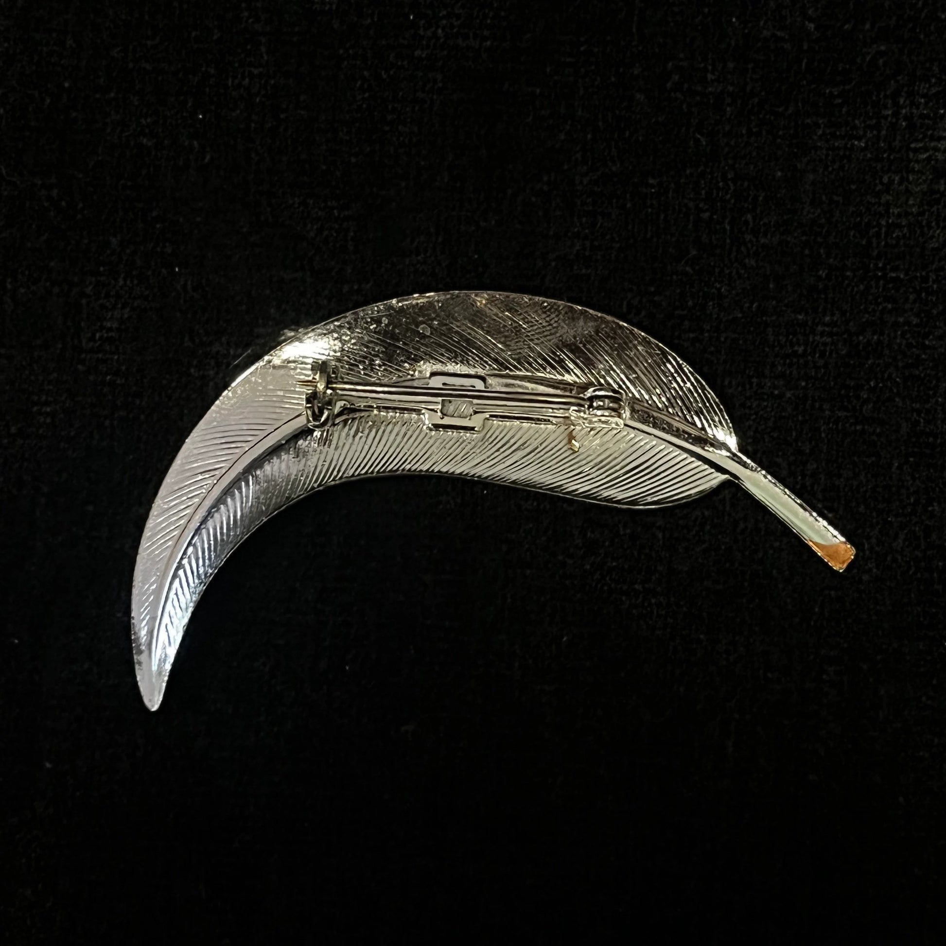 Silver feather-shaped brooch on a black background