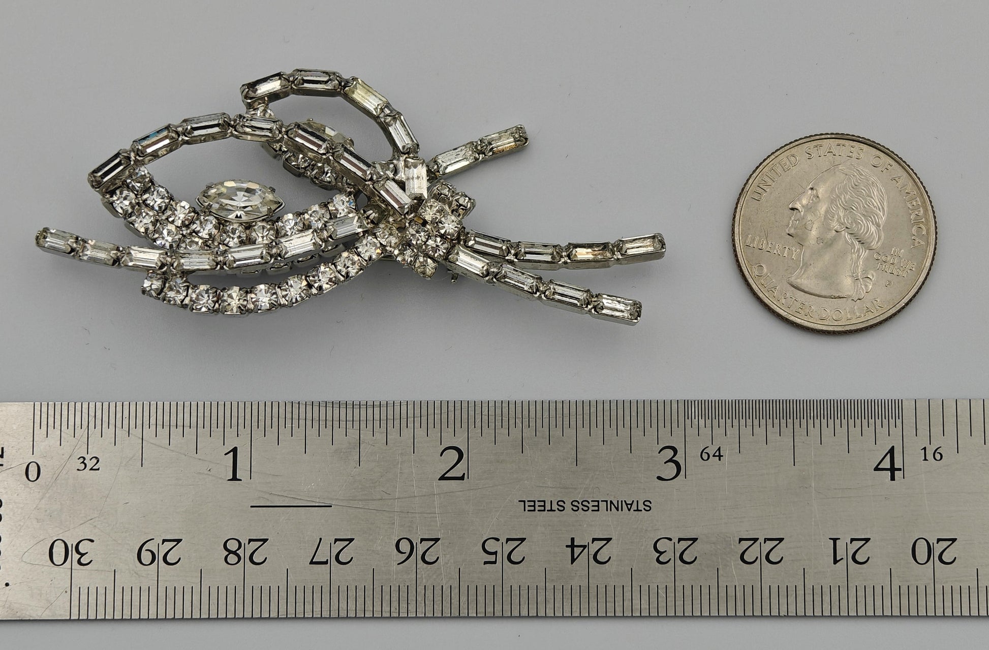 Silver brooch with gemstones next to a ruler and quarter for scale on a gray background