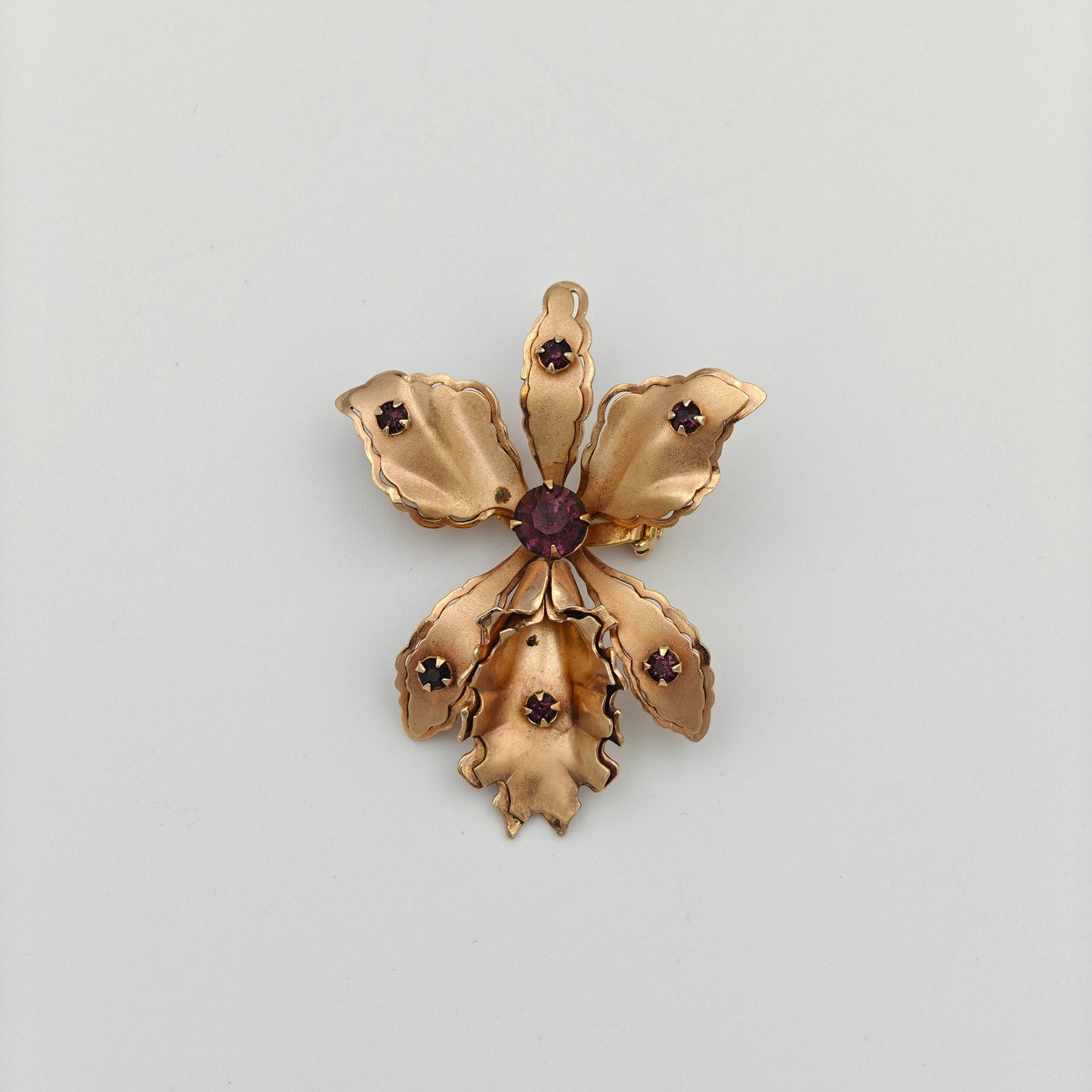 Gold flower-shaped brooch with a central red gemstone on a white background