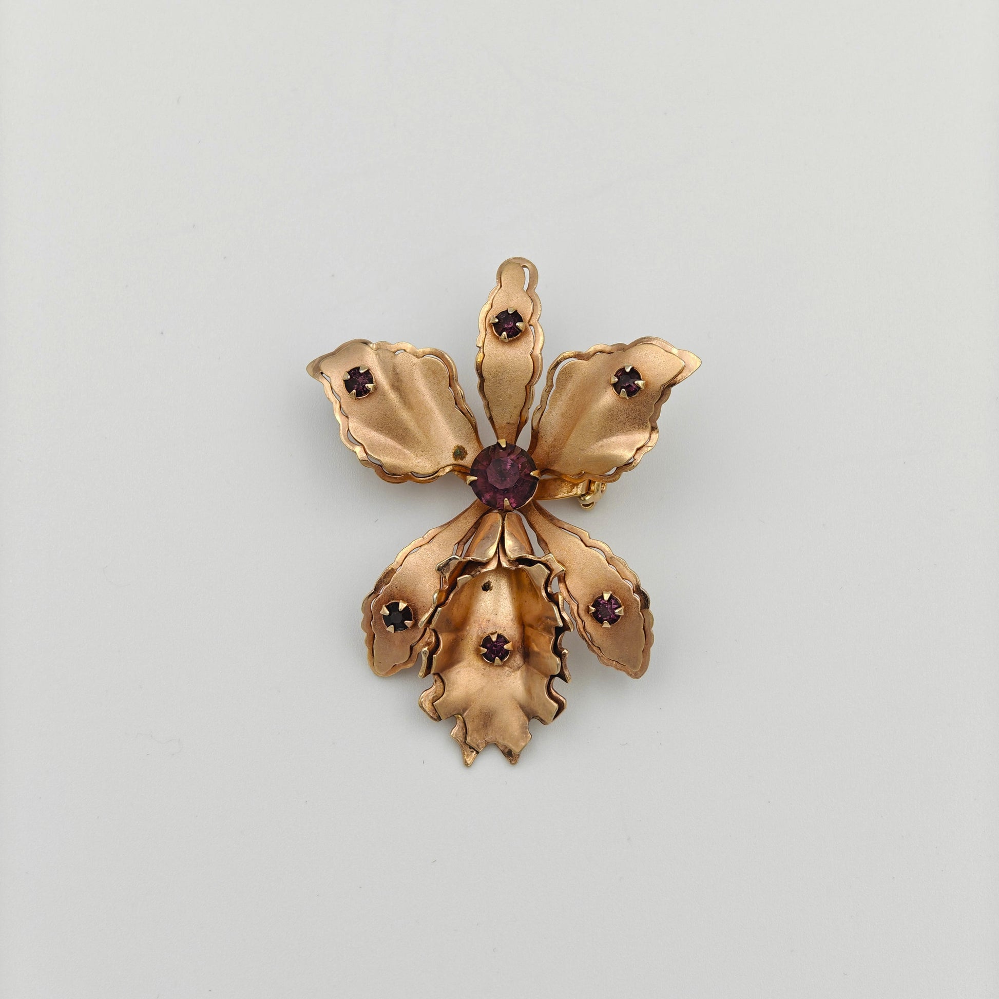 Gold flower-shaped brooch with a central red gemstone on a white background