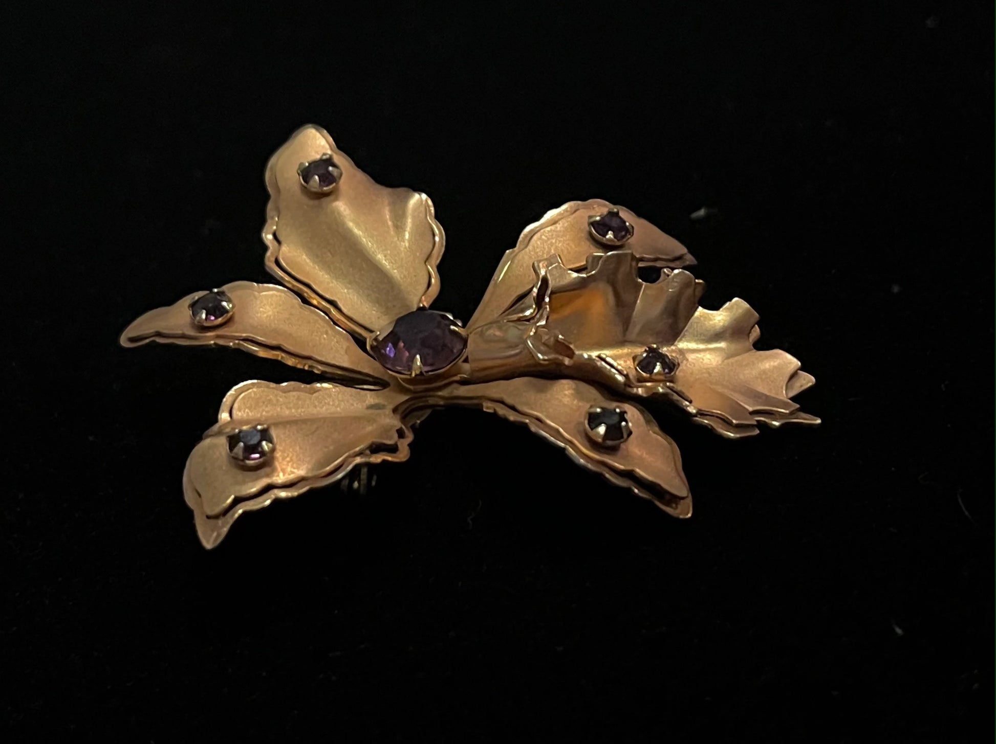 Gold flower-shaped brooch with embedded stones on a black background