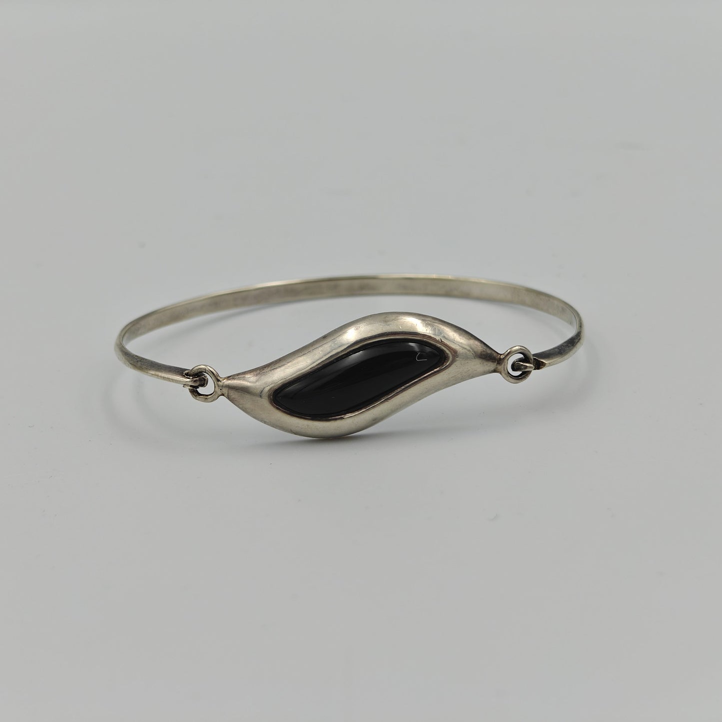 Silver bracelet with wavy central design with a black stone in the center on a white background.