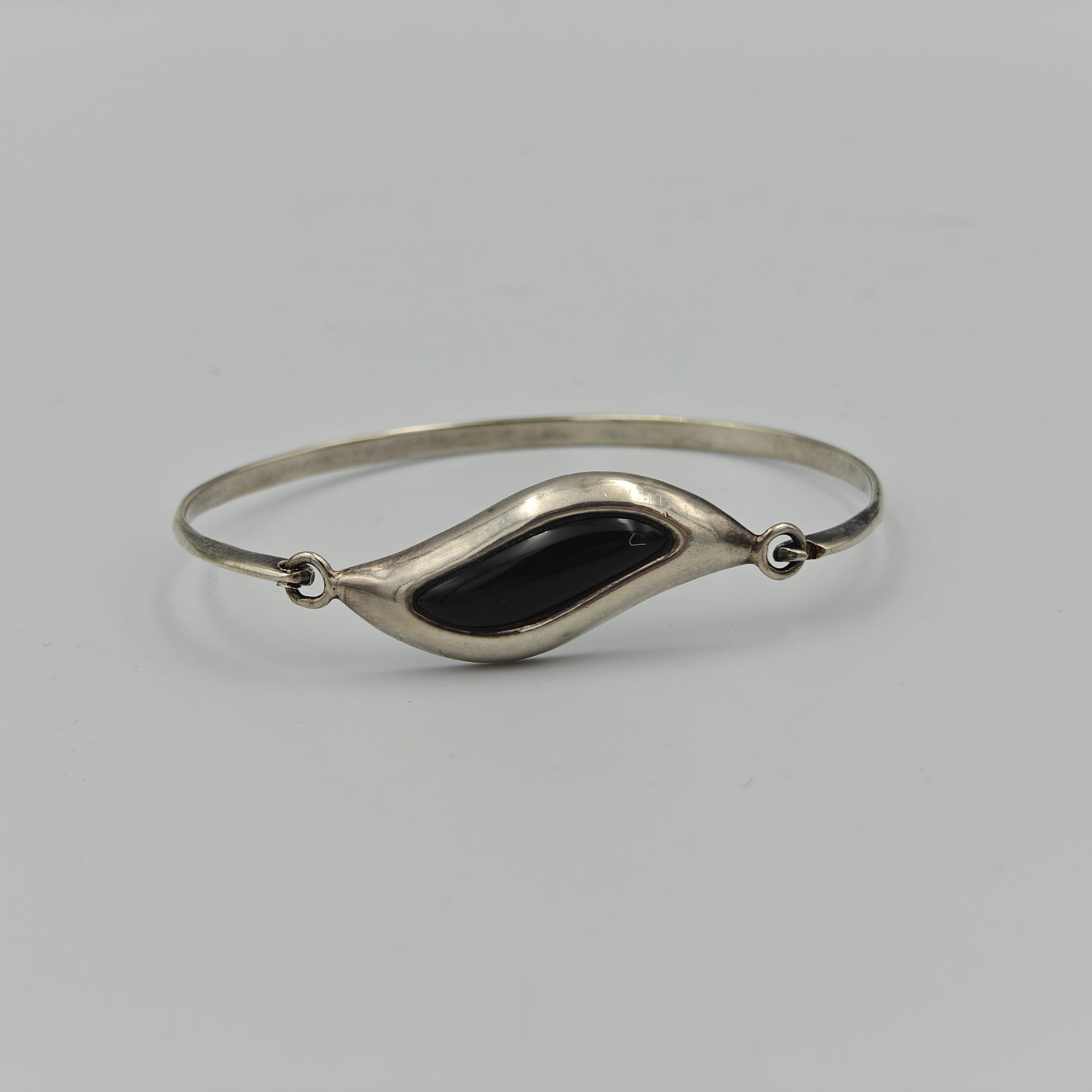 Silver bracelet with wavy central design with a black stone in the center on a white background.