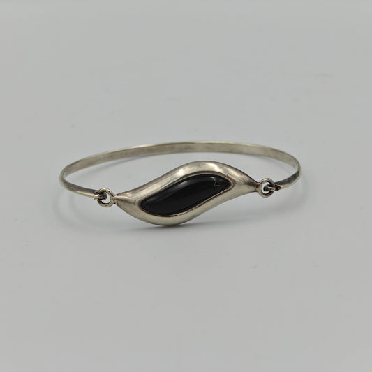 Silver bracelet with wavy central design with a black stone in the center on a white background.