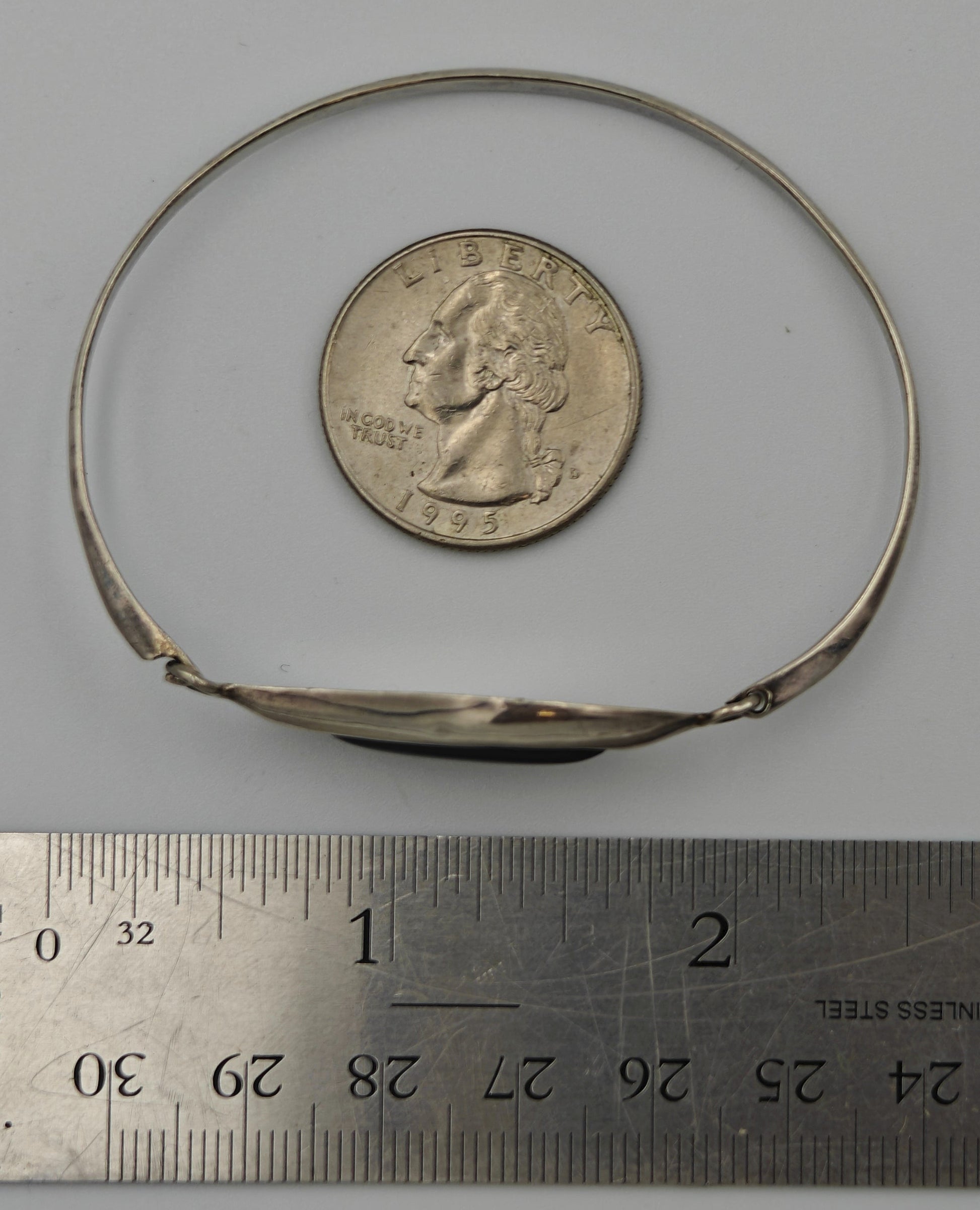 Silver bracelet next to quarter and ruler for scale on a white background.
