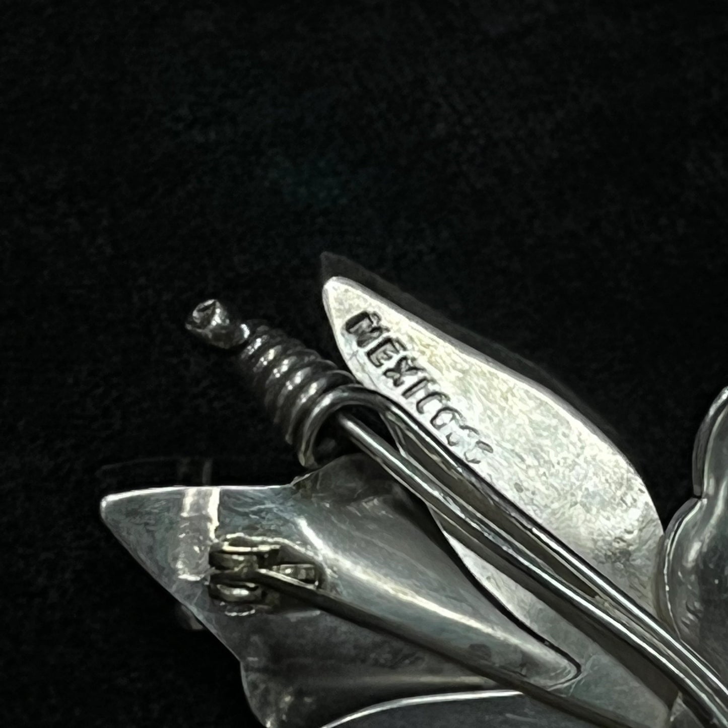Close-up of a silver brooch with 'Mexico' stamp on a black background