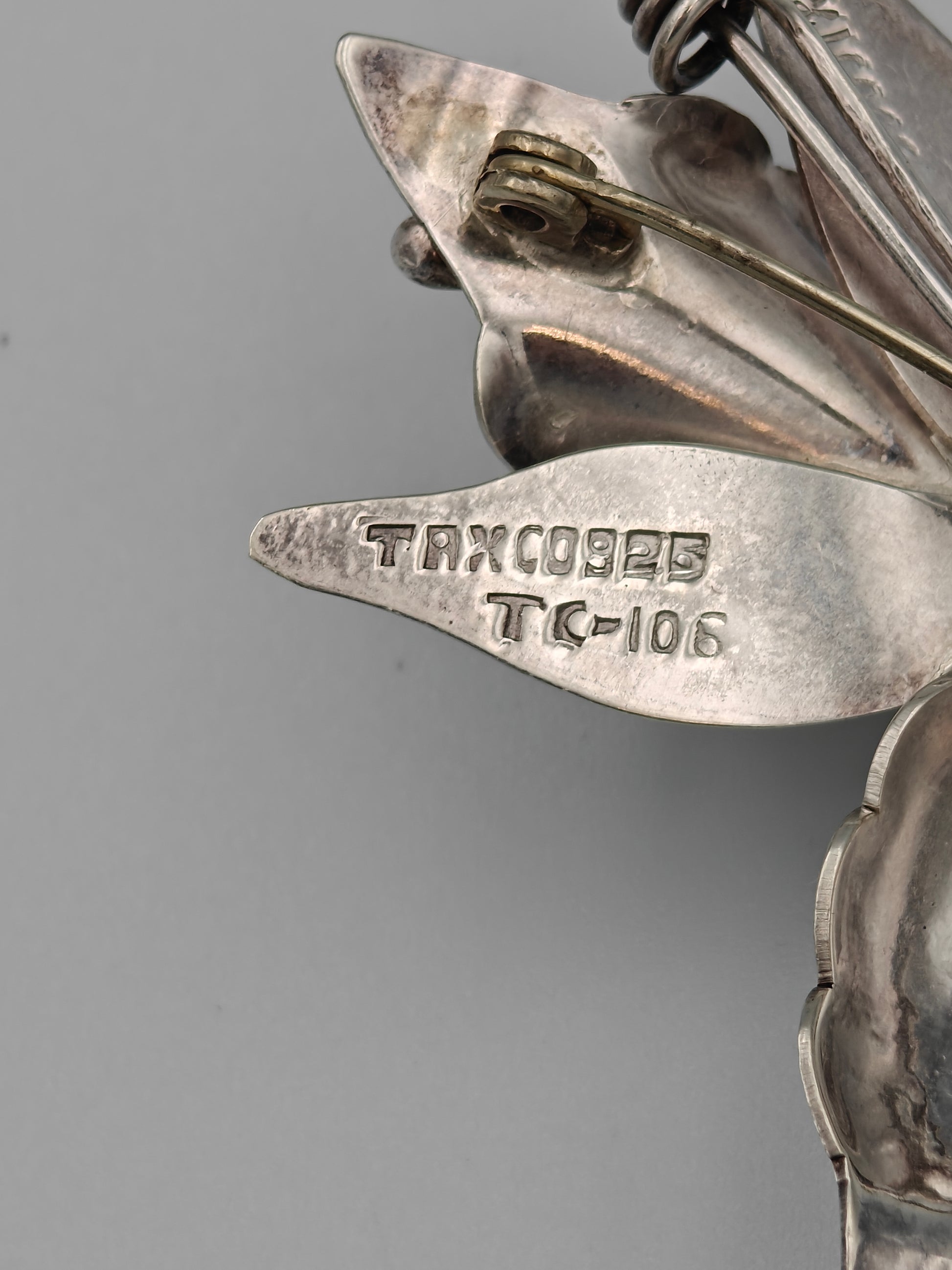 Close-up of a silver brooch with 'Taxco' engraving on a gray background
