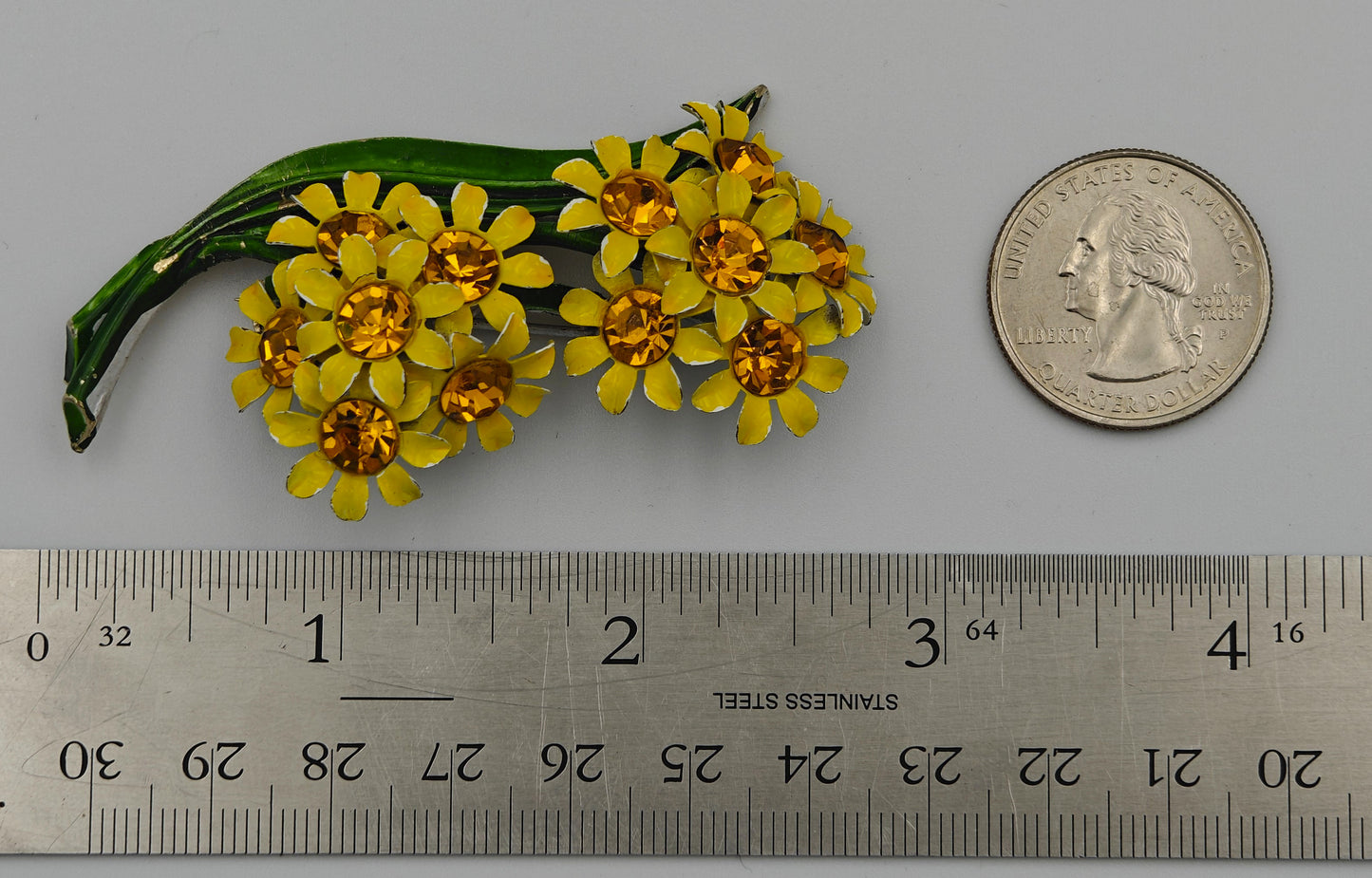Yellow flower brooch next to a ruler and coin for size reference