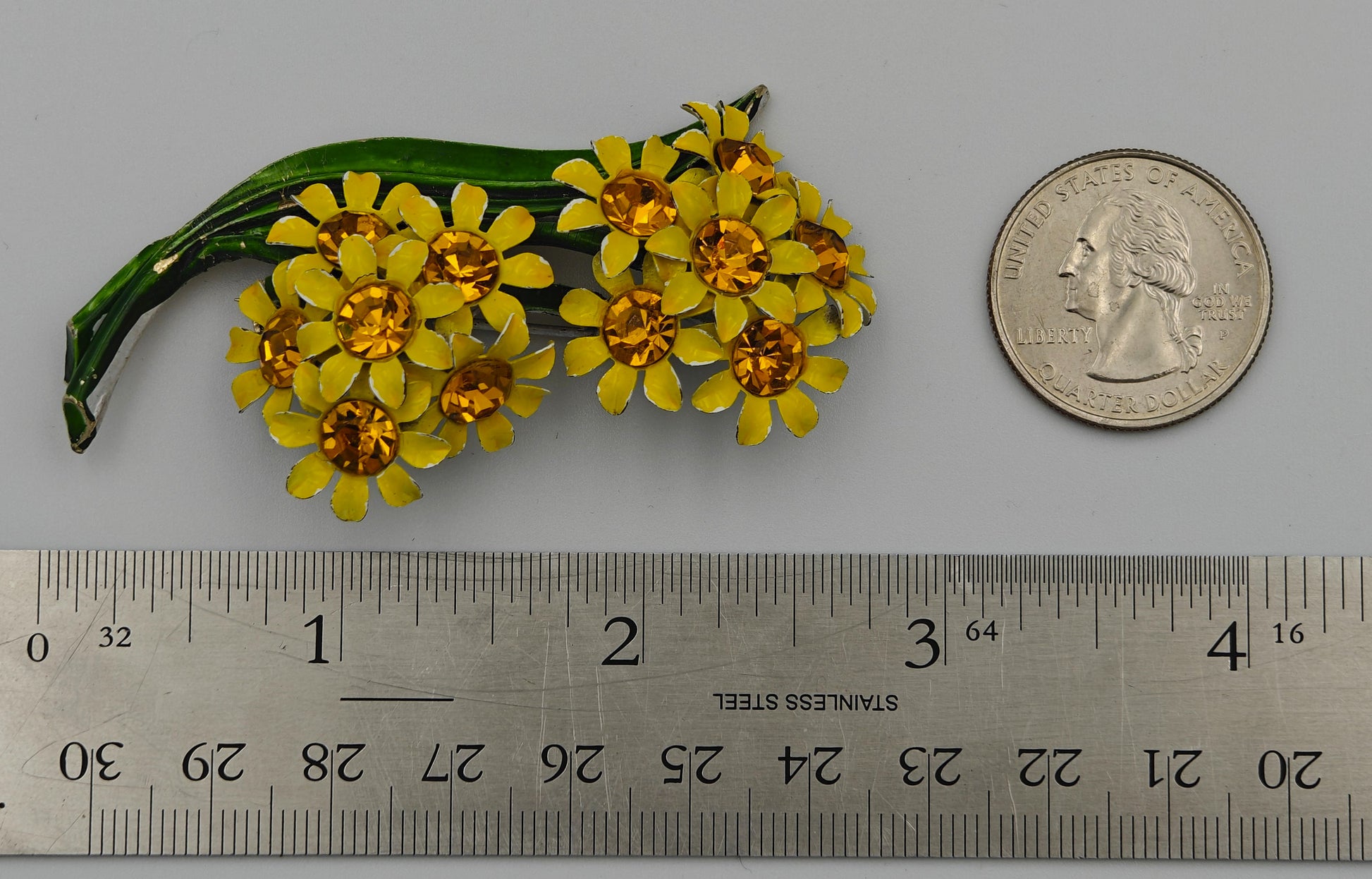 Yellow flower brooch next to a ruler and coin for size reference